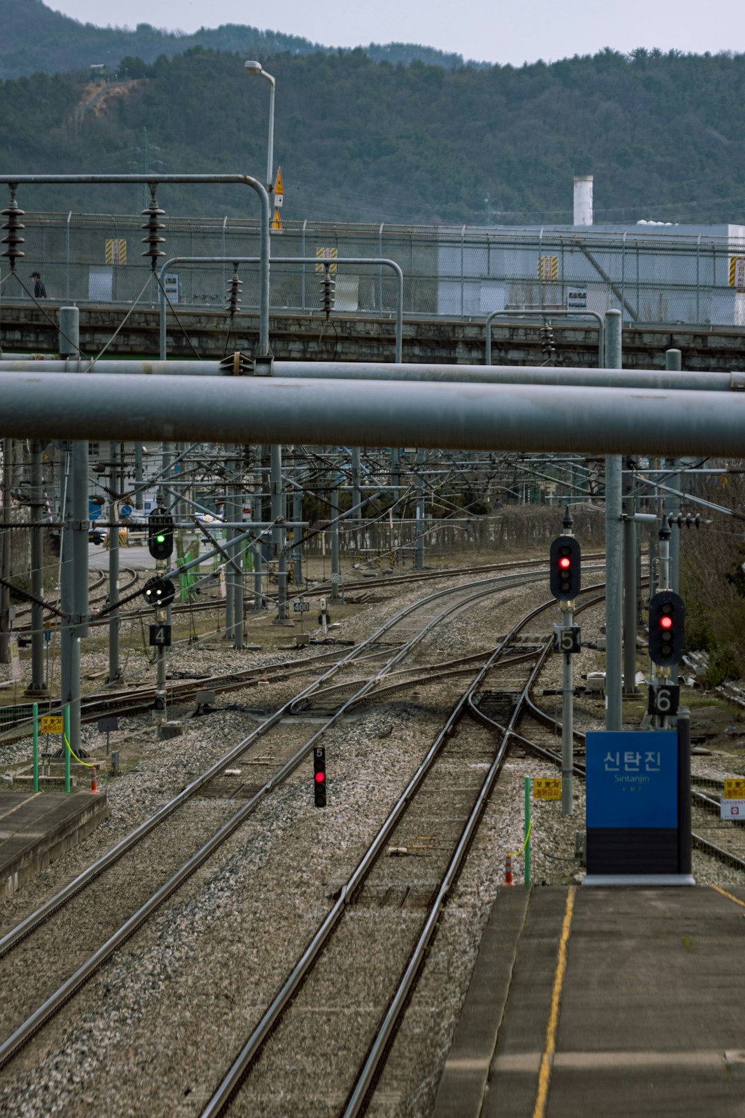 Multiple railway tracks converge near industrial structures and a station platform.